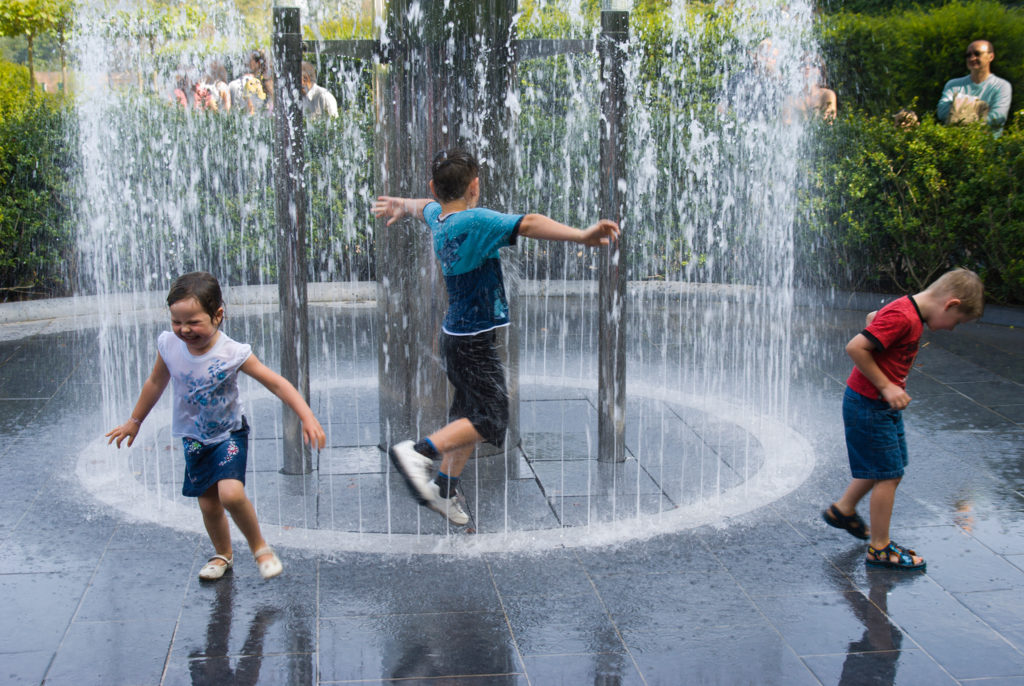 Children run into a fountain released by build up of a head of water visible in a tube popular water feature in Alnwick Garden Northumberland UK