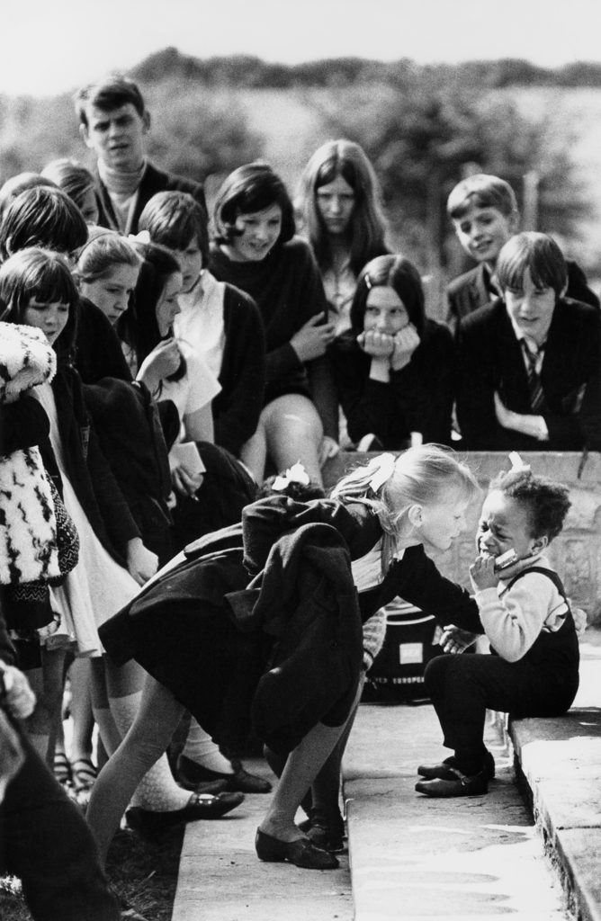 Vintage 1969 black and white print scan secondary school pupils crowd round a little black girl who has fallen and is crying at Maltby Grammar School sports day. Note the black child was one of twins from the only coloured family in this Yorkshire mining town and at this time there was no discrimination just a lot of attention.